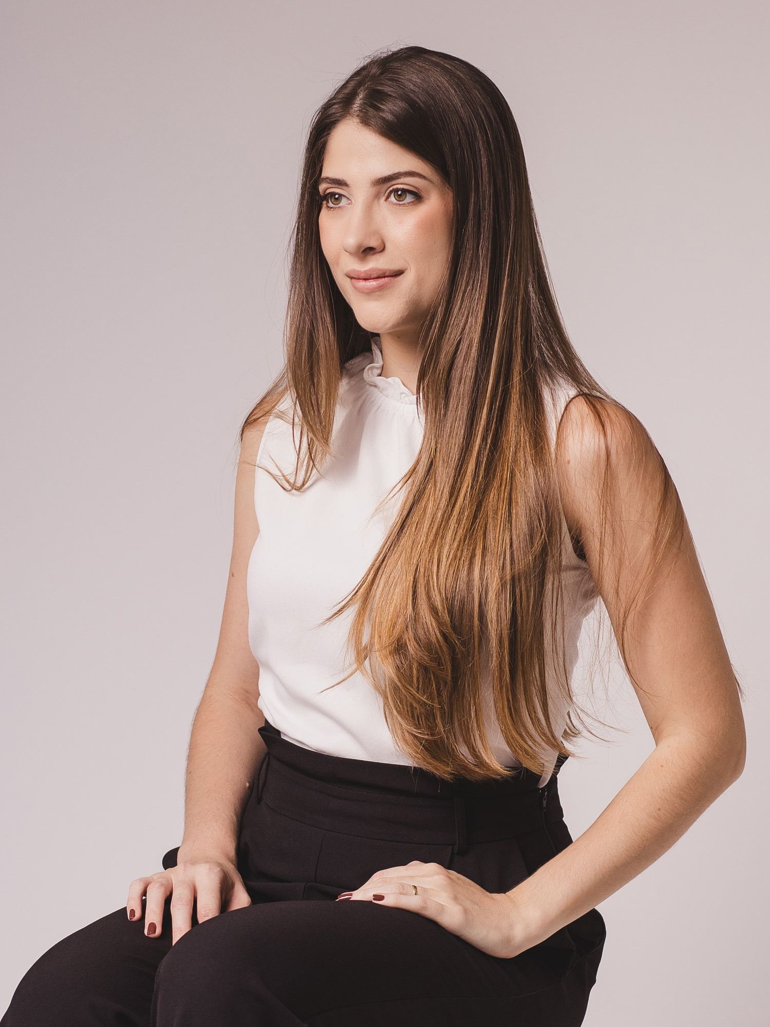 Caroline Firmino sentada, com as mãos apoiadas sobre o joelho, olhando para o lado.